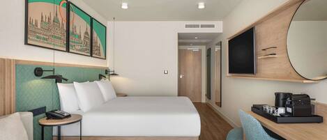 Une chambre d’hôtel comprenant un lit, un bureau avec une machine à café, une chaise, une petite table et un grand miroir.