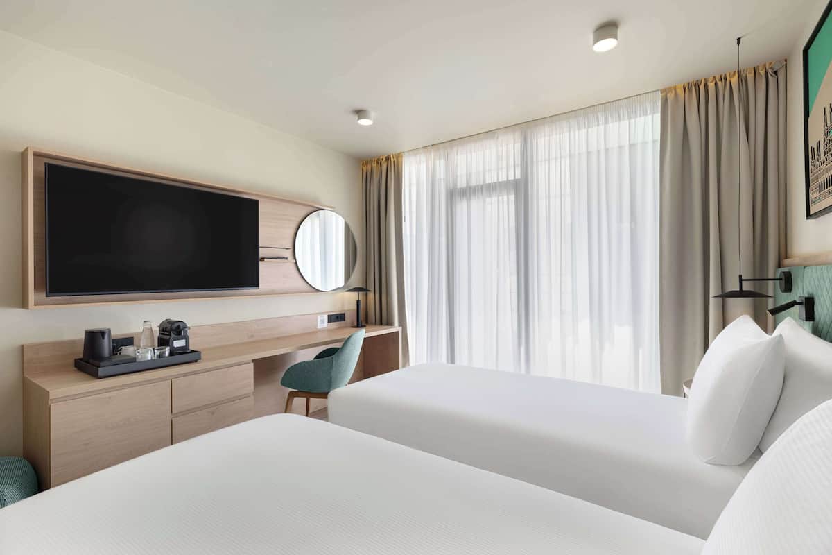 Habitación de hotel con una cama grande, un escritorio con computadora, televisión y ventana con cortinas.