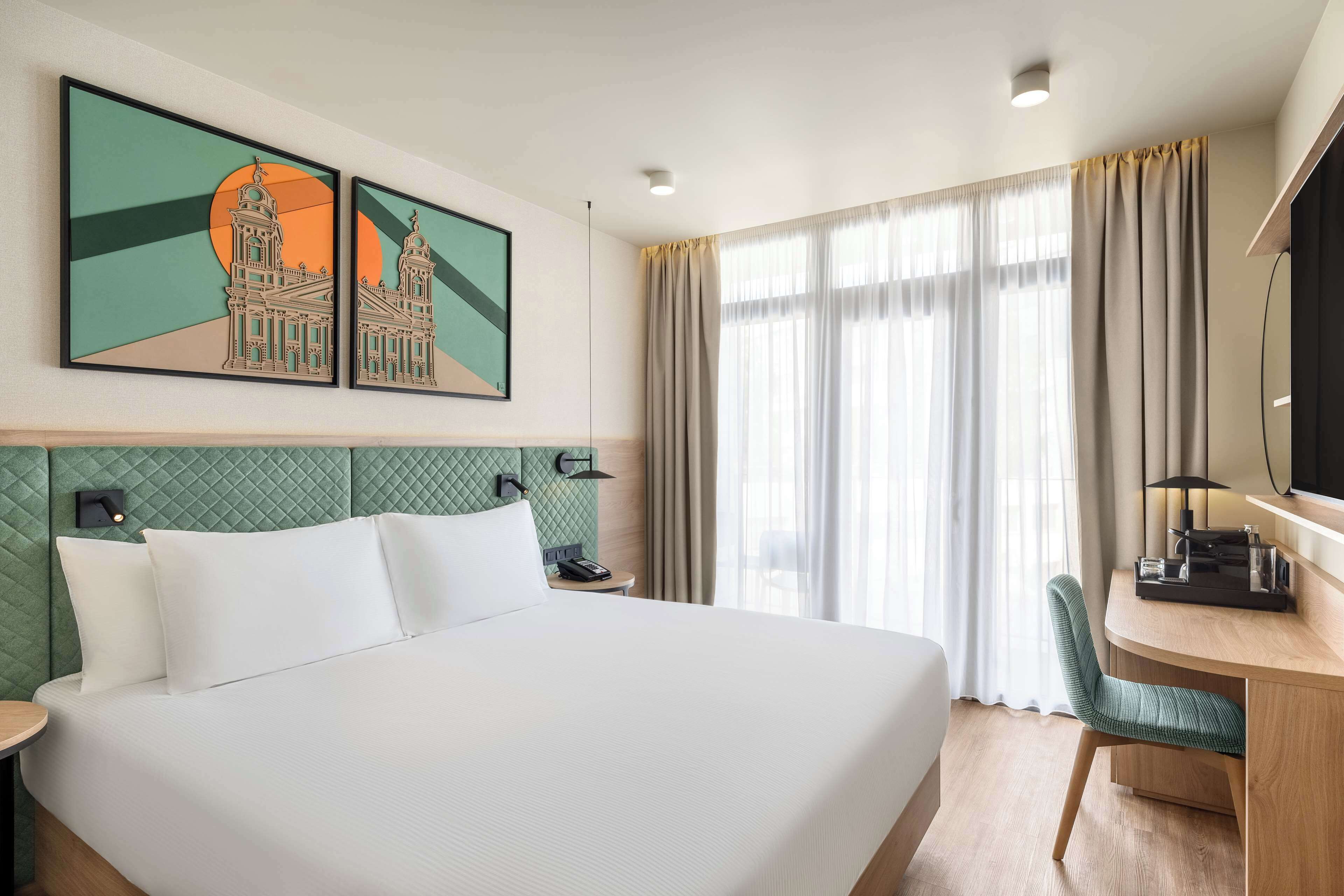 Une chambre d’hôtel avec un grand lit, un bureau avec une chaise, une télévision et deux œuvres d’art encadrées au mur.