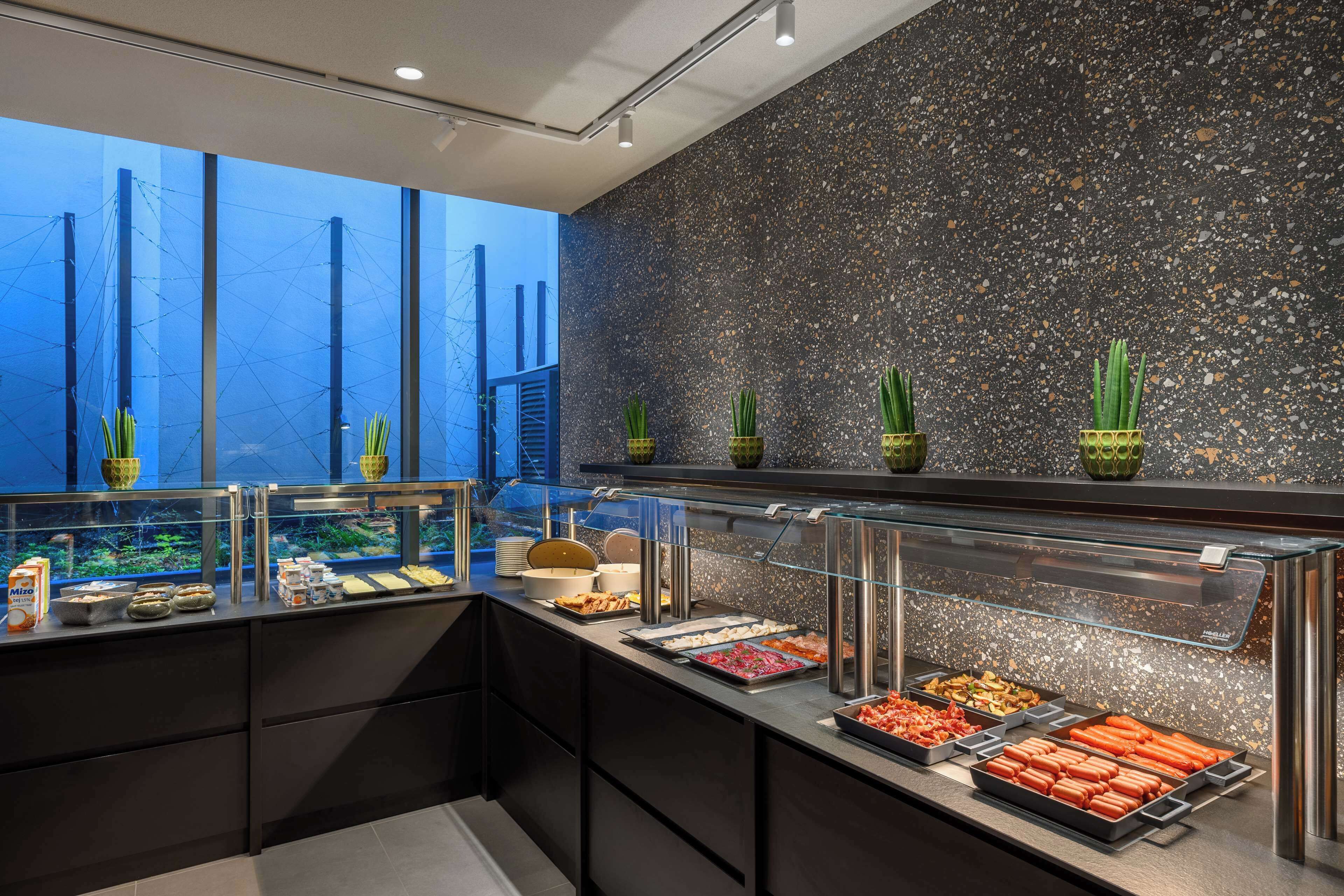Ein Buffet mit verschiedenen Speisen, eine Glastheke und Blick auf die Stadt durch große Fenster.