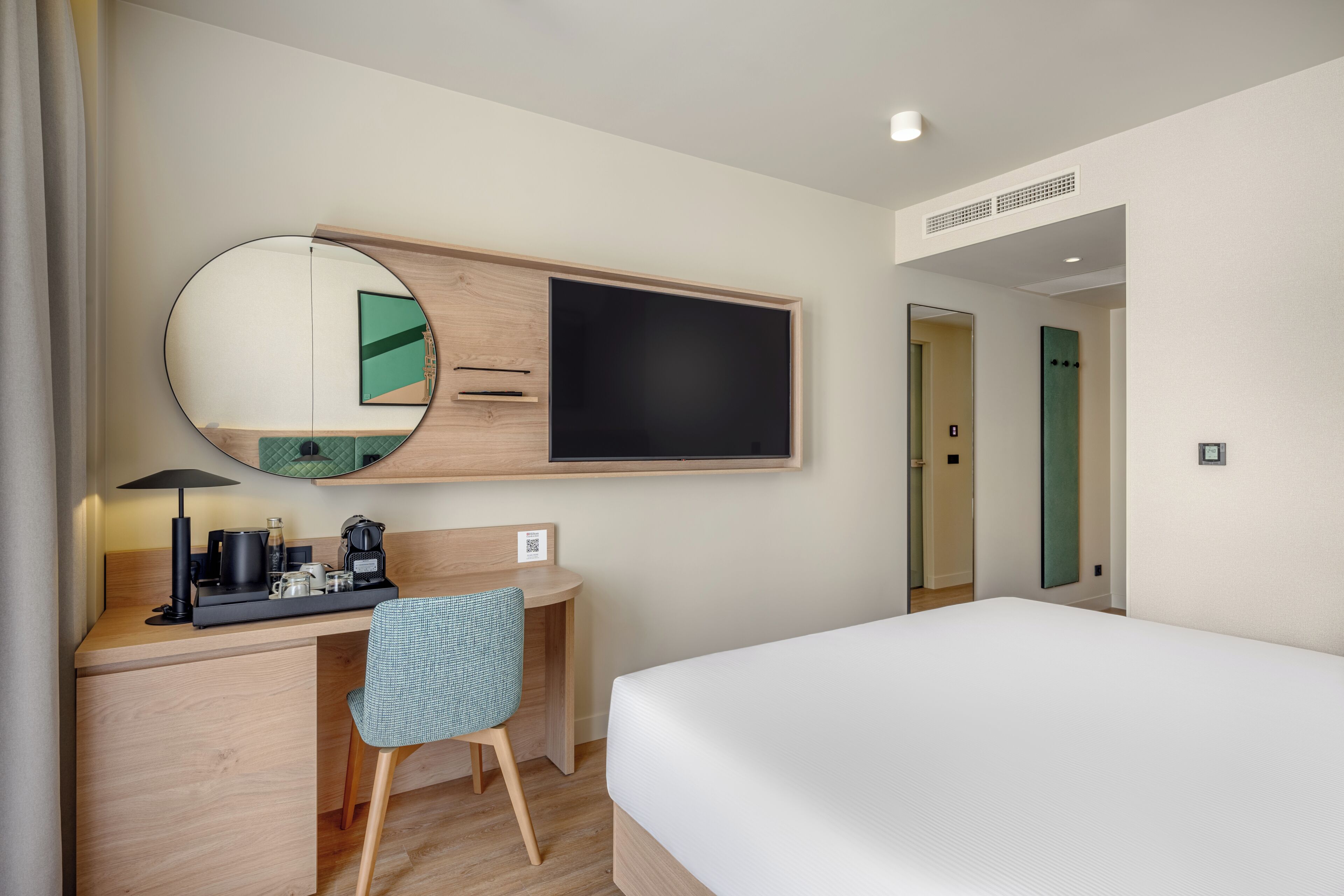 A hotel room with a bed, desk, chair, and a large mirror.