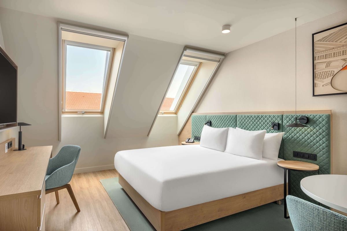 Una habitación de hotel moderna con una cama grande, un escritorio y dos ventanas.
