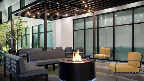 A modern outdoor seating area with a circular fire pit, cushioned benches, and chairs. - Home2 Suites By Hilton Athens I 65 (Athens)