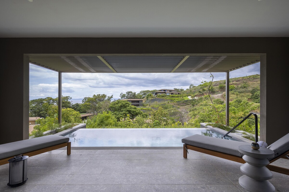 A spa area with two loungers and a hot tub, overlooking a hilly landscape.