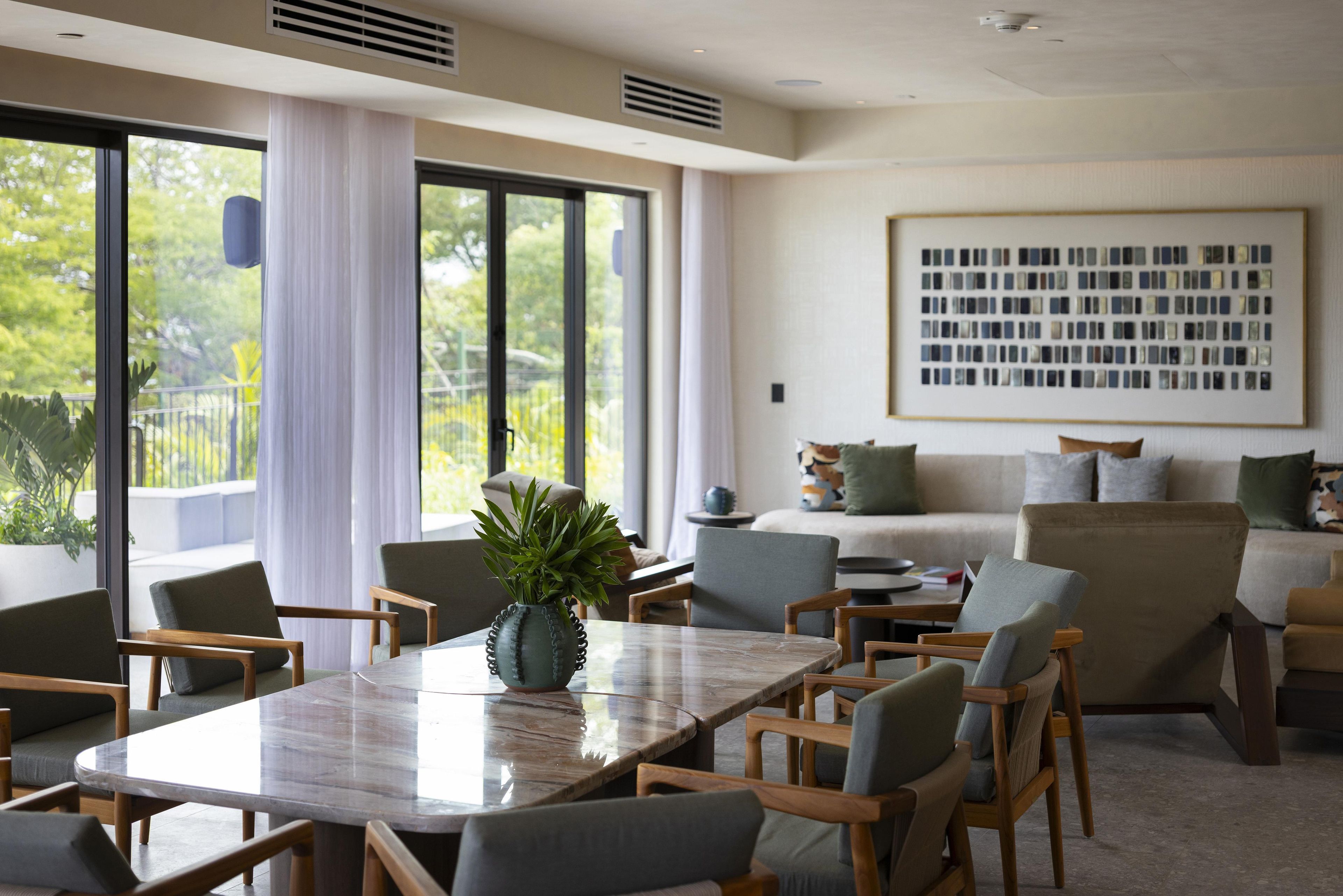 A modern hotel room with a dining area, a sofa set, and a large window with curtains.