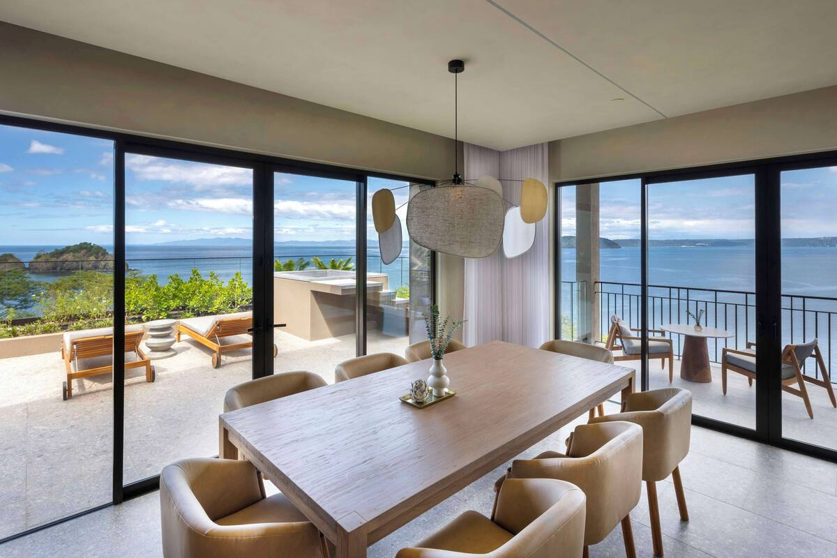 A spacious dining area with a large table and comfortable seating, overlooking a scenic ocean view.