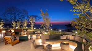 An outdoor seating area with a curved sofa, chairs, and a fire pit, surrounded by trees and overlooking a body of water. - Waldorf Astoria Costa Rica Punta Cacique (Sardinal)
