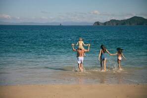 A beach scene with a man carrying a child and two women walking towards the water. - Waldorf Astoria Costa Rica Punta Cacique (Sardinal)