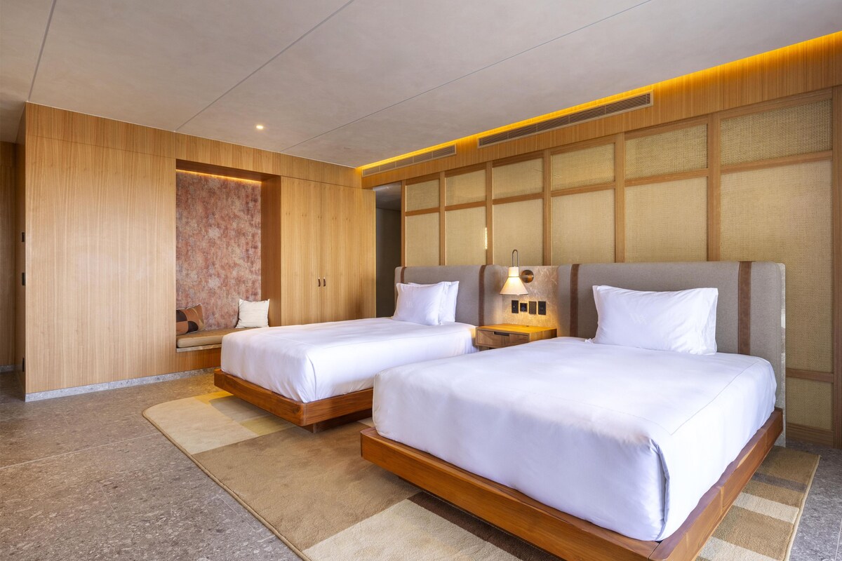 A hotel room with two beds, a seating area, and a large window.