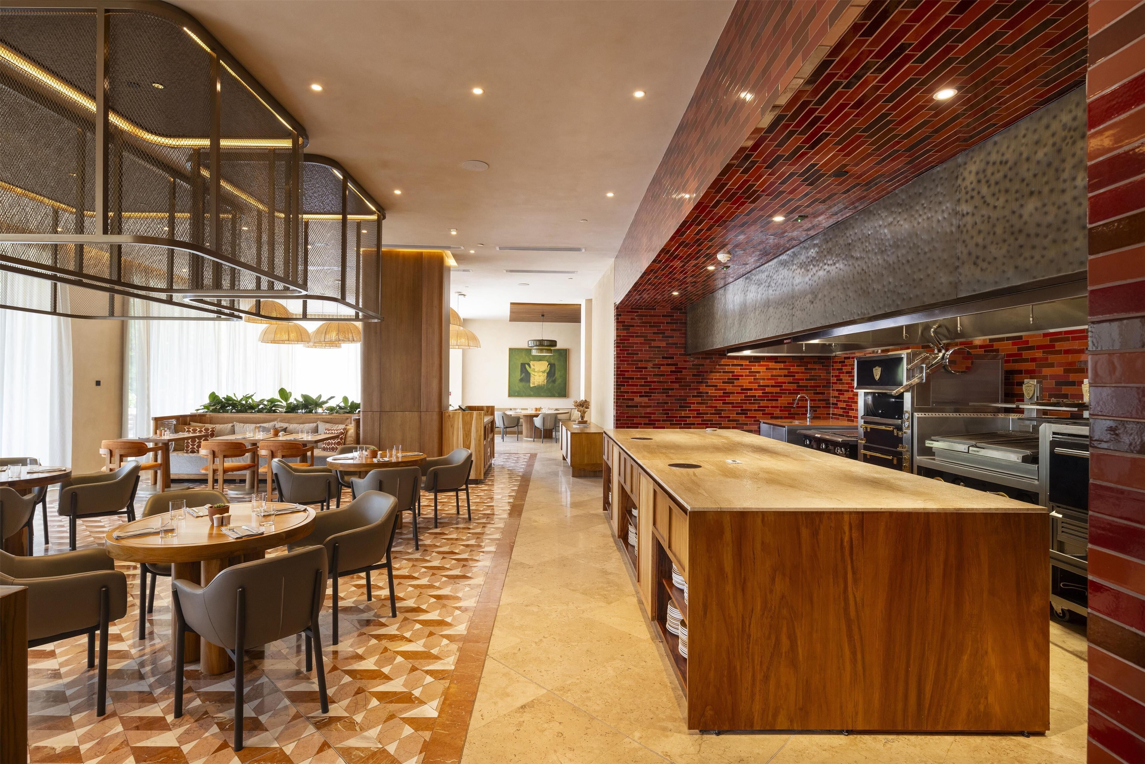 A modern restaurant with a central island, seating around it, and a brick accent wall.