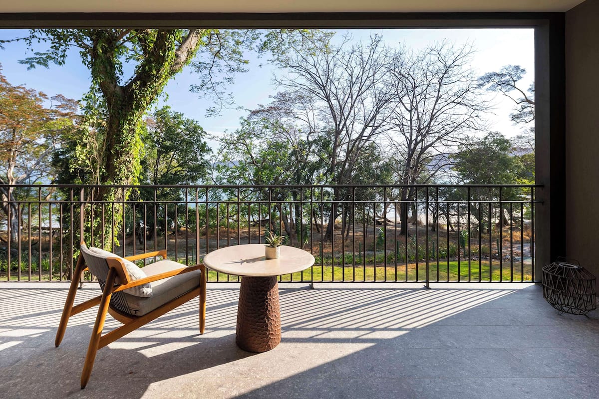 A balcony with a table and chair, a view of trees, and a metal railing.