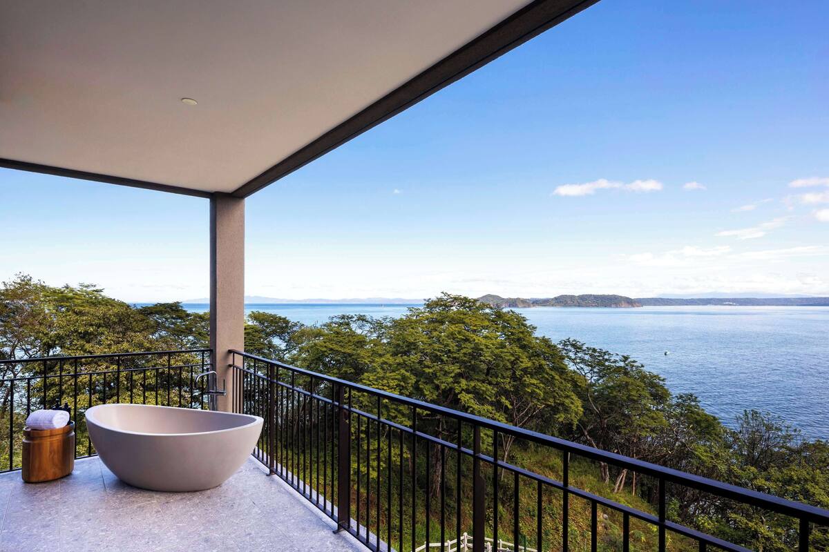 A balcony with a large bathtub, a wooden stool, and a metal bucket.