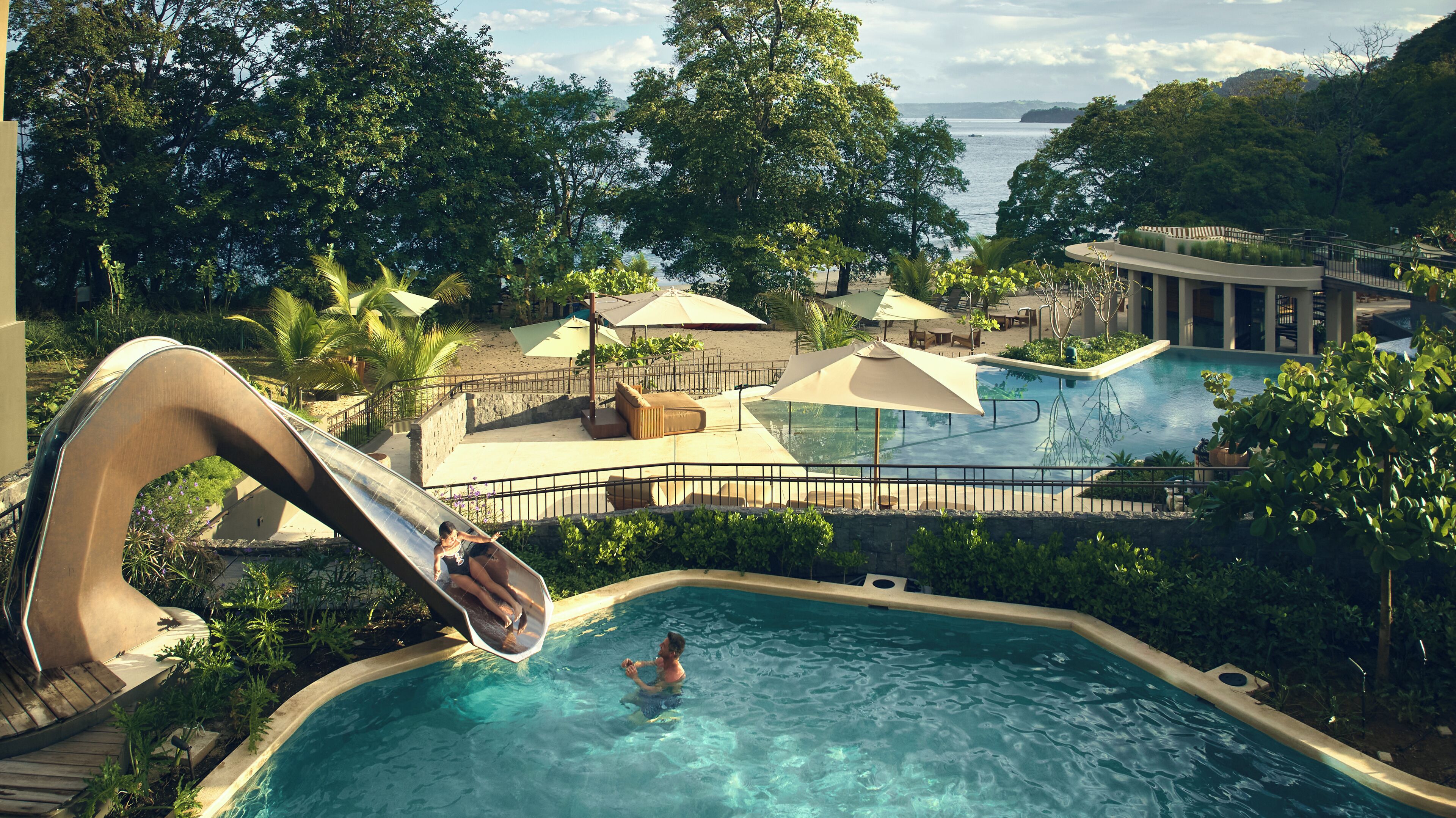 A pool area with a slide, lounge chairs, umbrellas, and a view of the sea.