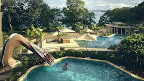 A pool area with a slide, lounge chairs, umbrellas, and a view of the sea. - Waldorf Astoria Costa Rica Punta Cacique (Sardinal)
