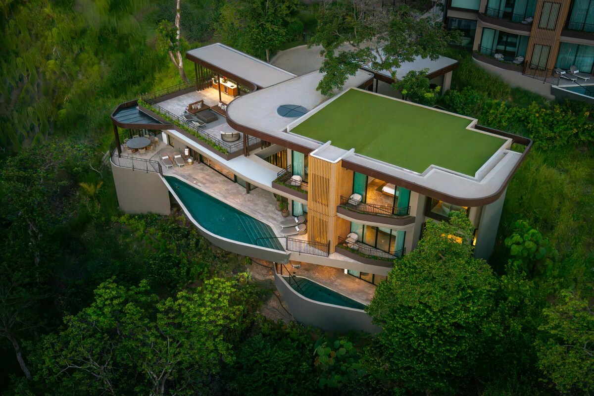 A modern multi-story house with a swimming pool, outdoor seating, and lush greenery.