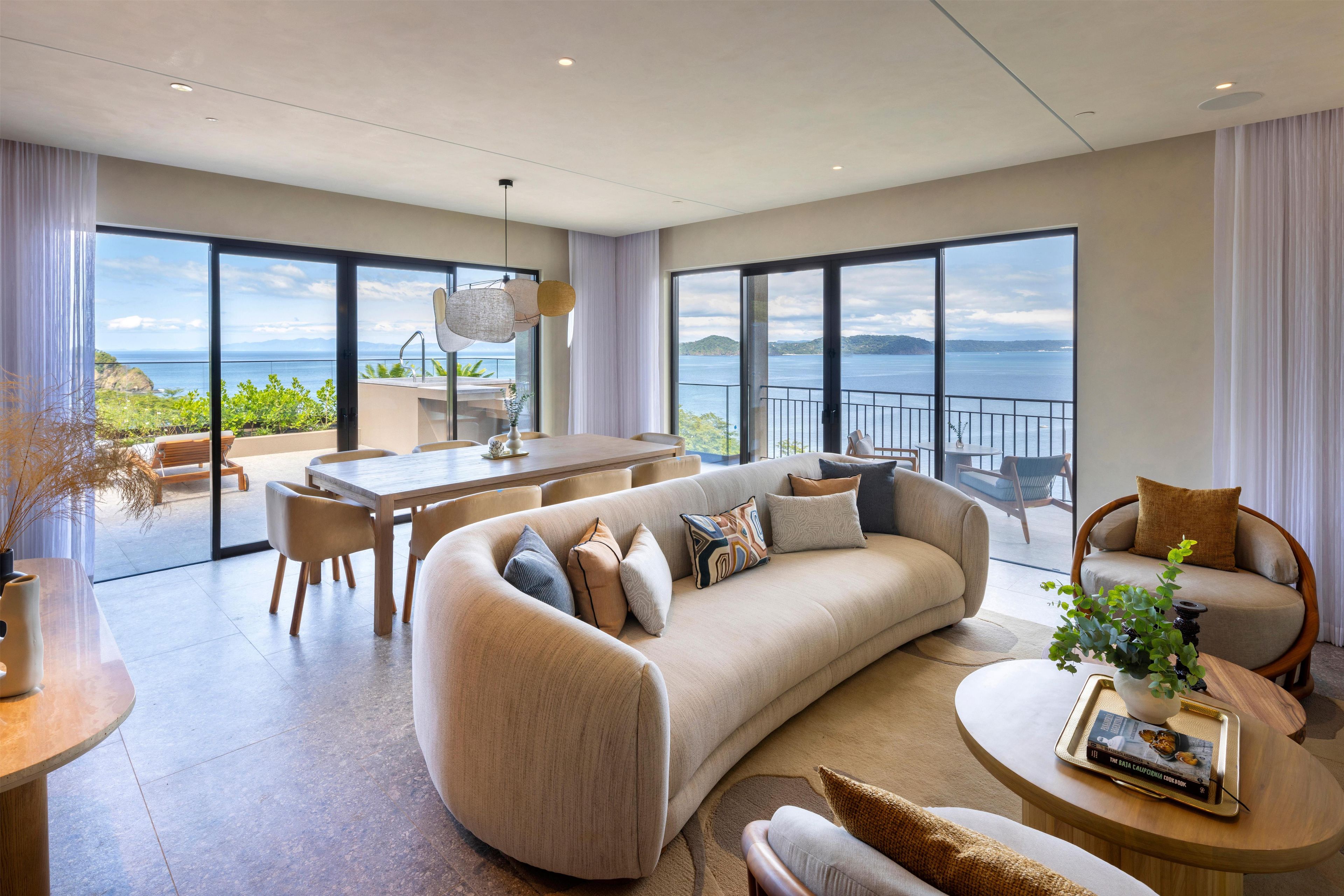 A spacious living area with a large sofa, a dining table, and a view of the sea.