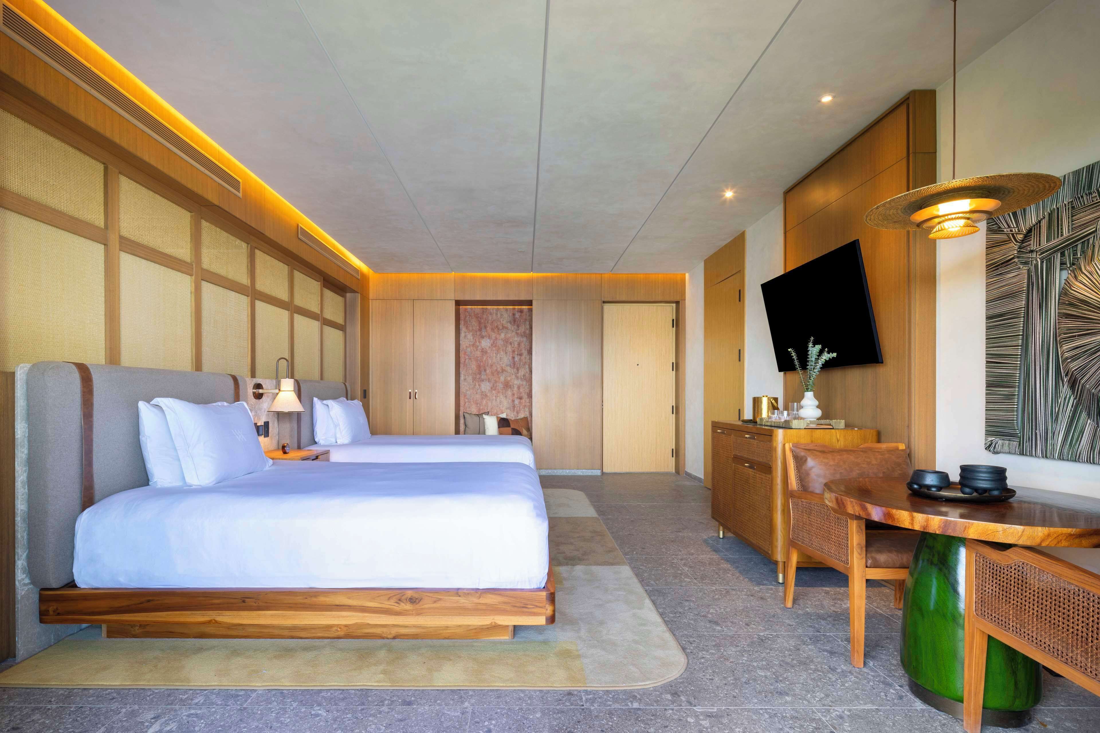 A hotel room with two beds, a desk, a chair, a television, and a large window.