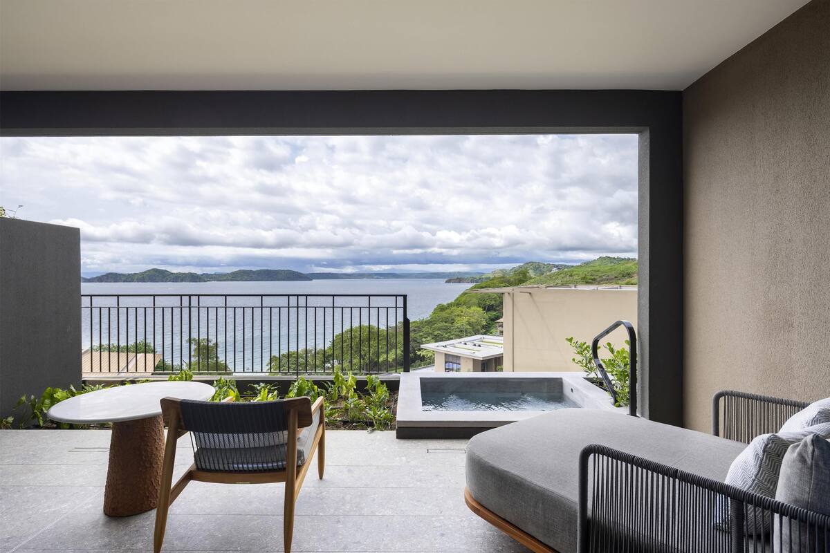 A balcony with a view of the sea, a hot tub, and a seating area.