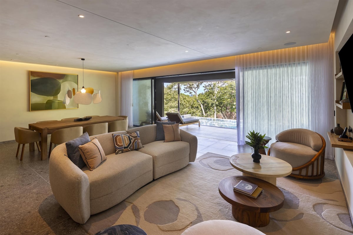 Un salon moderne comprenant un canapé, une table basse et des fauteuils, un coin repas avec une table et des chaises, ainsi que de grandes fenêtres avec des rideaux.
