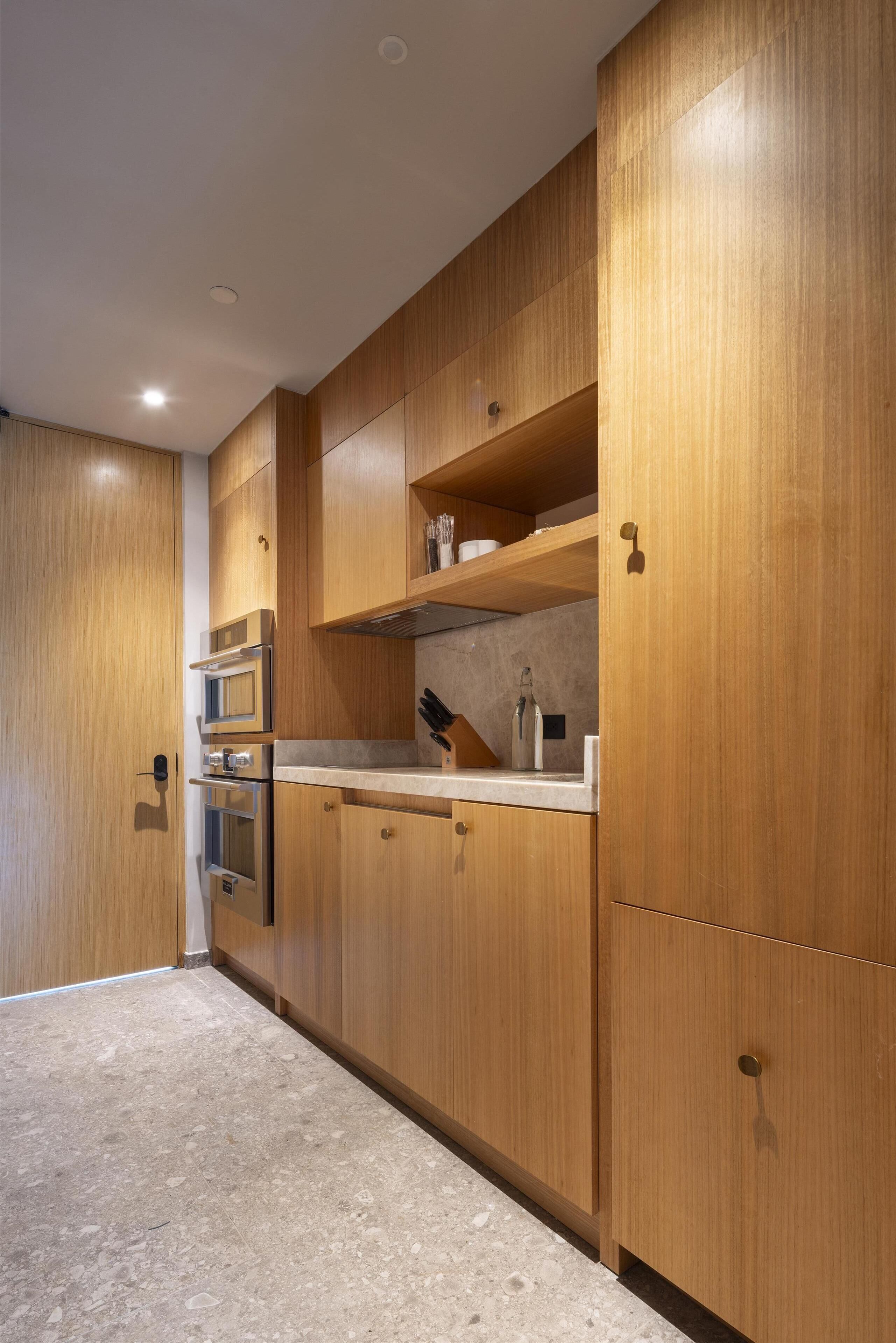 A modern kitchen with wooden cabinetry, stainless steel appliances, and a marble countertop.