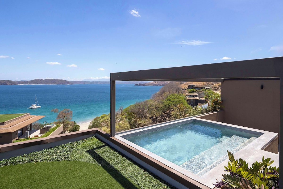 Une piscine à débordement moderne offrant une vue dégagée sur l’océan et les collines lointaines.