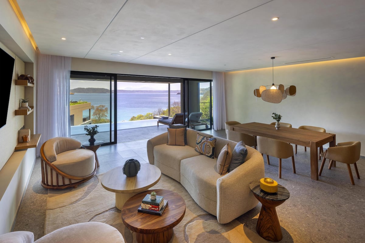 A modern living room with a large window, a dining area, and a sofa set.