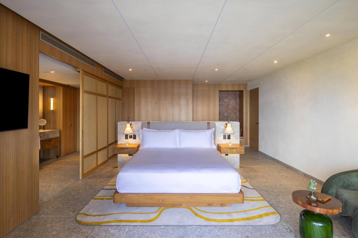 A modern hotel room with a large bed, wooden headboard, bedside lamps, and a television.