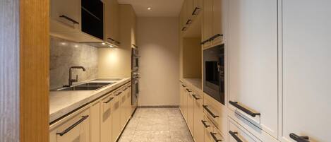 A narrow kitchen with beige cabinets, a marble countertop, and a black oven.