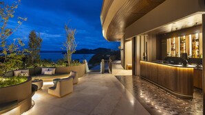 An outdoor seating area with a bar, overlooking a body of water and hills at dusk. - Waldorf Astoria Costa Rica Punta Cacique (Sardinal)