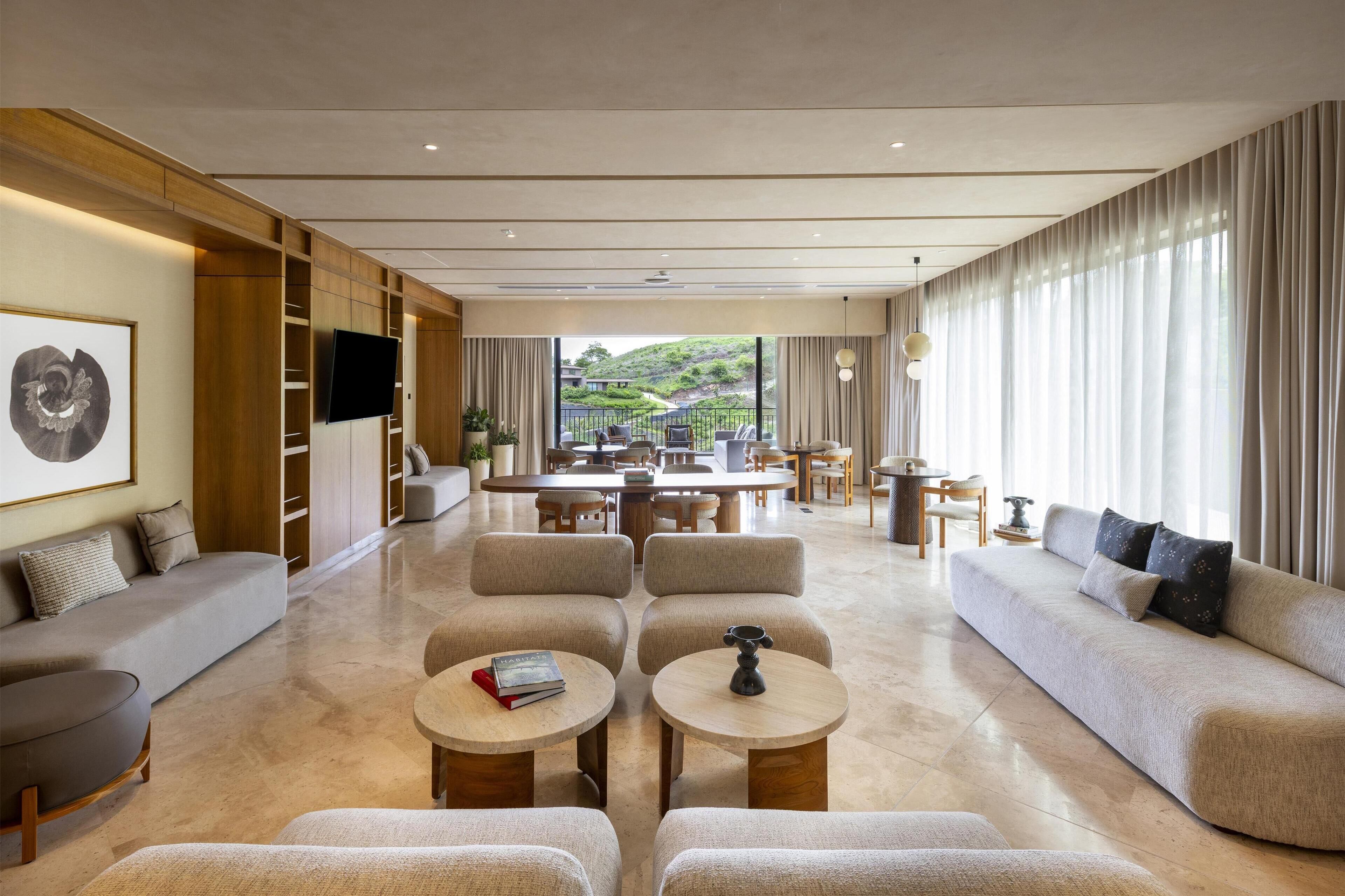 A spacious hotel lobby with a modern design, featuring a large seating area, a dining table, and a view of the outdoors.