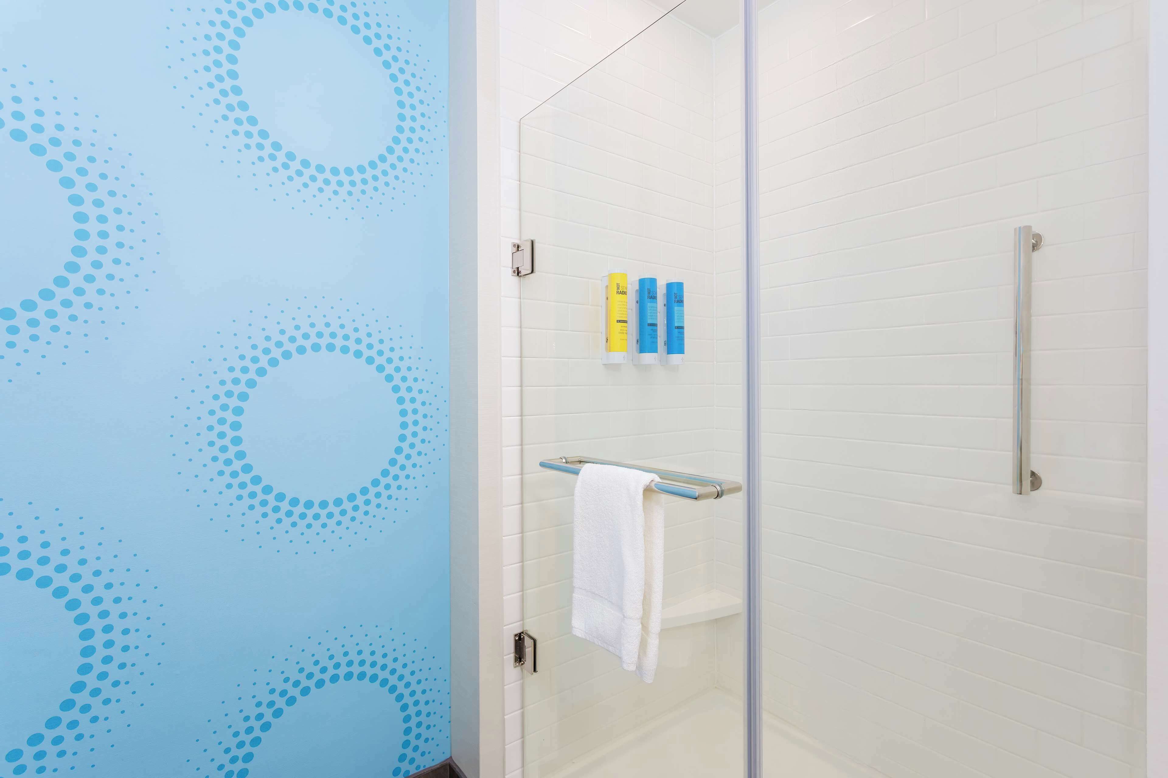 A bathroom with a glass shower door, white tiled walls, and a blue wall with a dotted pattern.