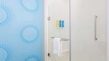 A bathroom with a glass shower door, white tiled walls, and a blue wall with a dotted pattern.
