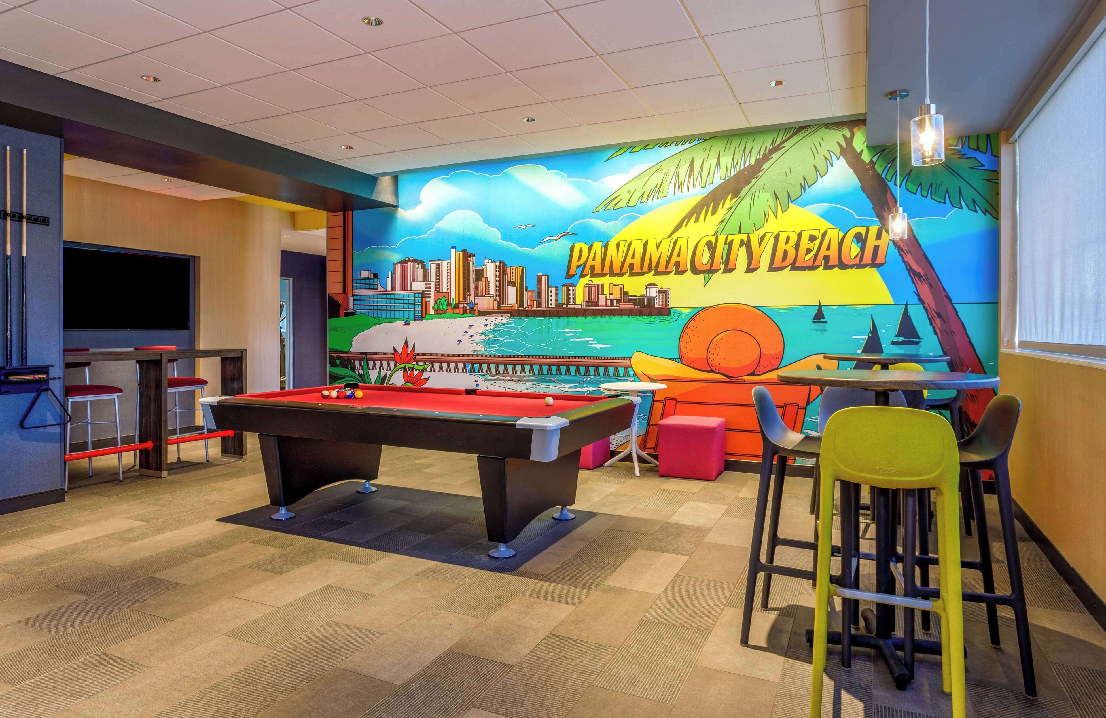 A pool table in a room with a mural of Panama City Beach, a bar area, and a television screen.