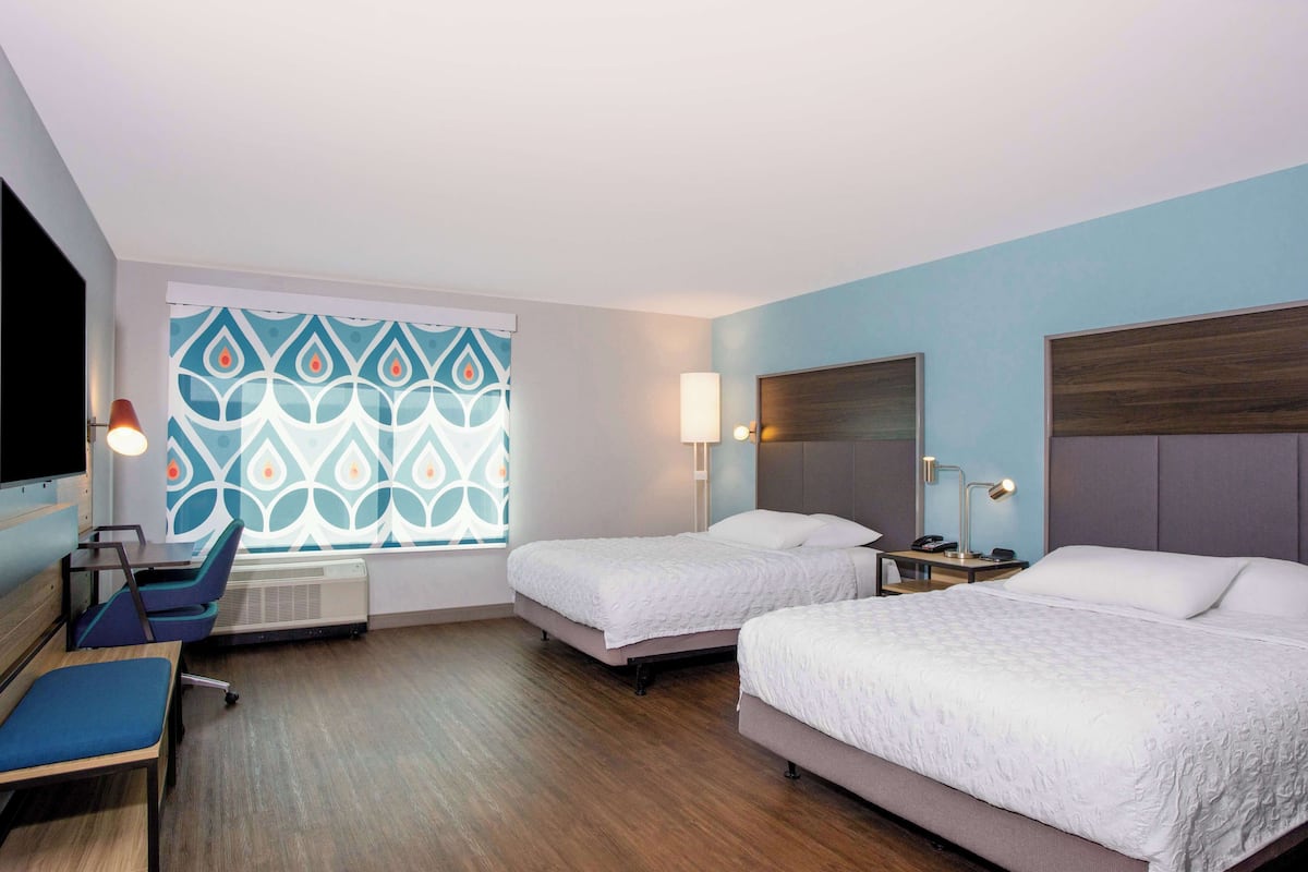 A hotel room with two beds, a desk, a chair, and a window with a decorative pattern.