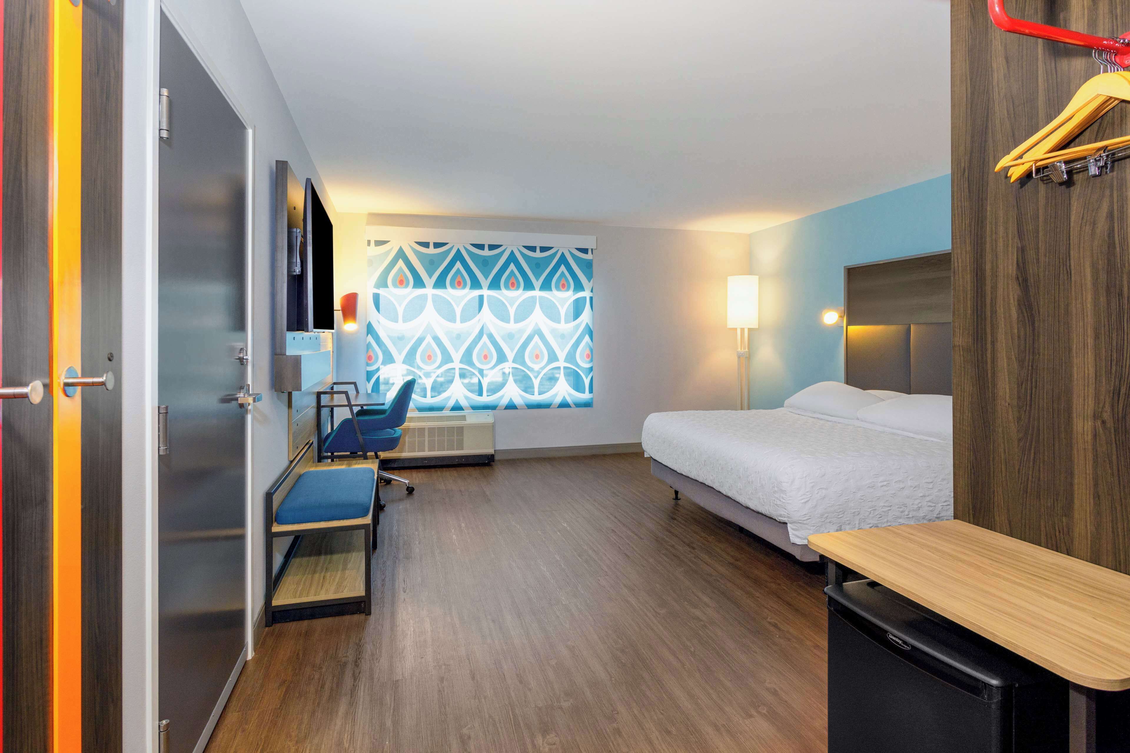 A hotel room with a bed, desk, chair, TV, and a patterned wall.