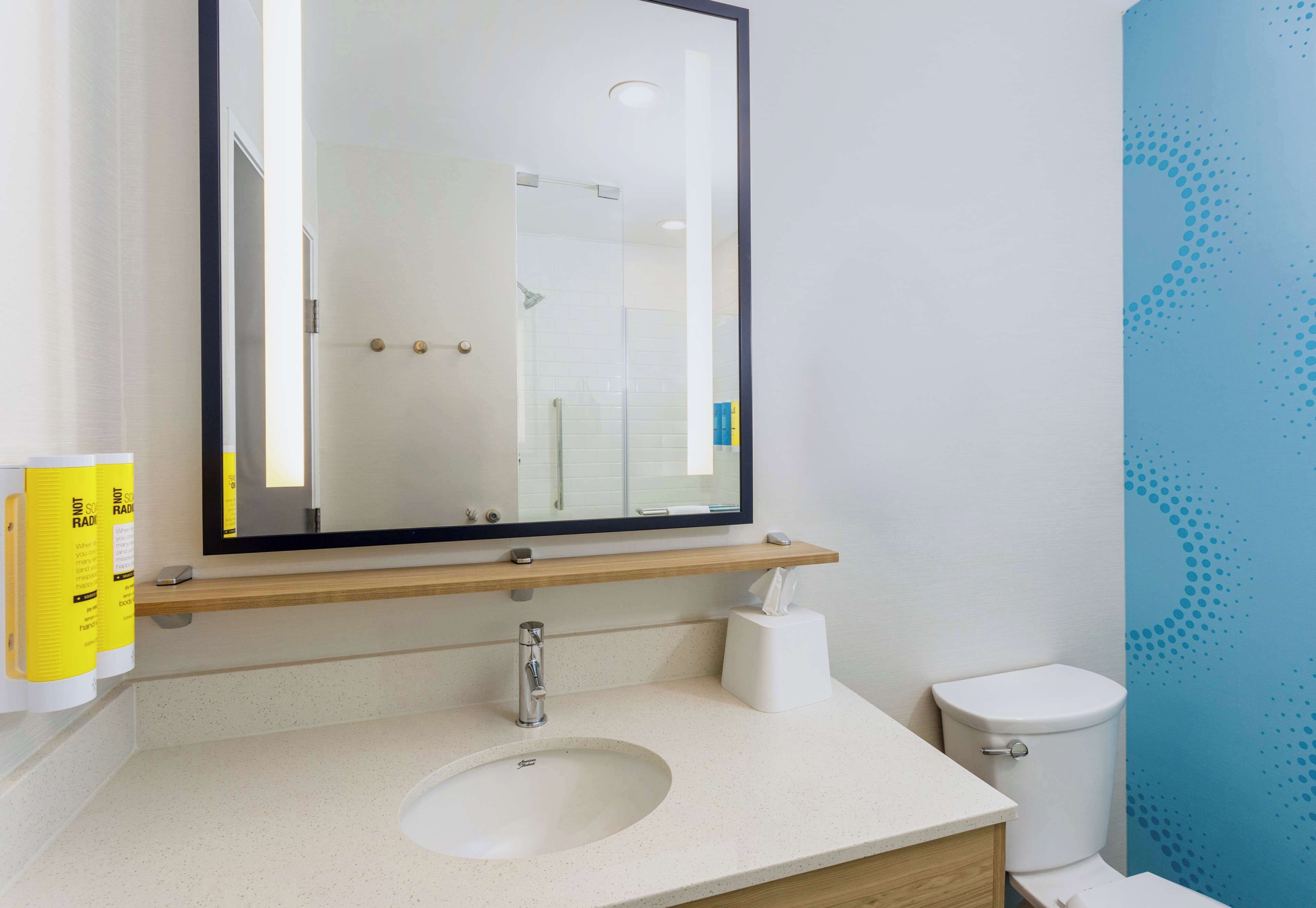 A modern bathroom with a large mirror, a sink, a toilet, and a towel dispenser.