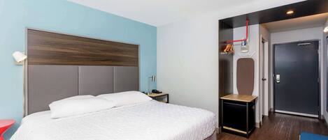 Une chambre d’hôtel moderne avec un grand lit, une table de chevet, une chaise rouge et une armoire avec un miroir.