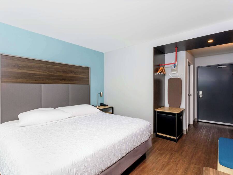 Una habitación de hotel moderna con una cama grande, una mesita de noche, una silla roja y un armario con espejo.