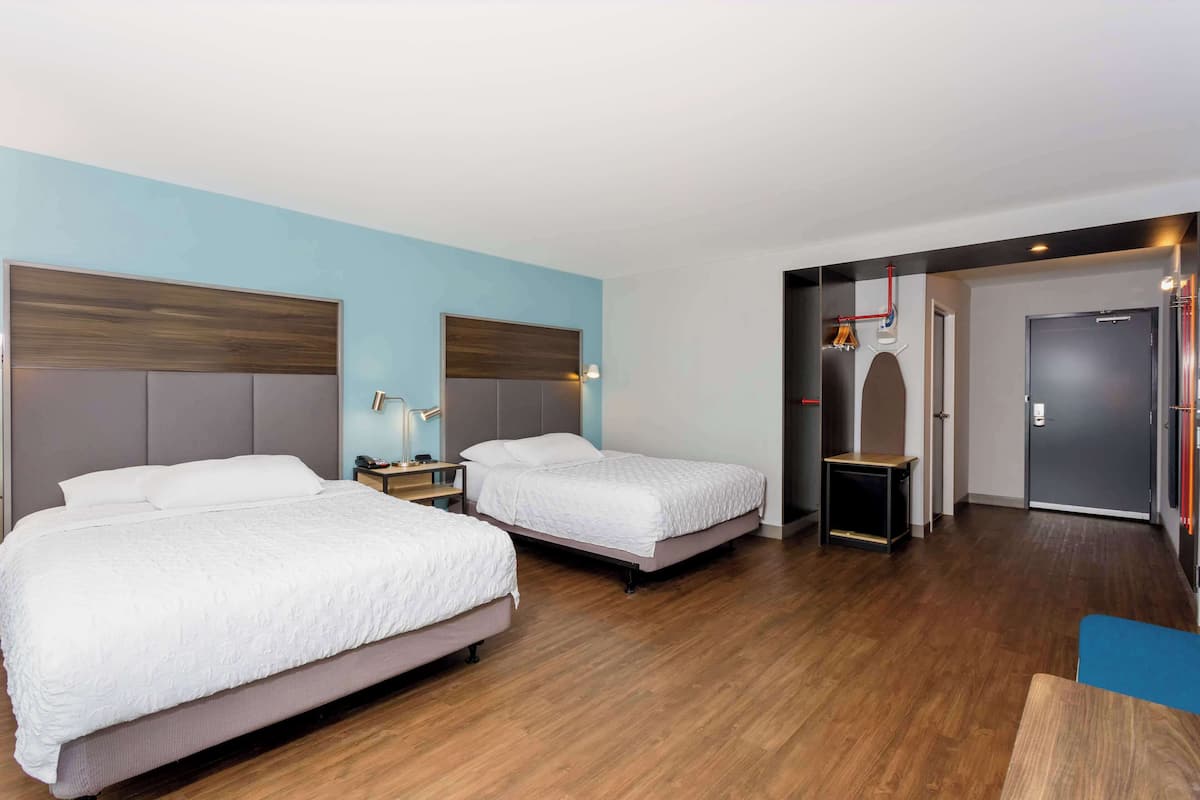 A hotel room with two beds, wooden flooring, and a modern design.