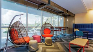 A modern lounge area with a large window, a hanging chair, a cushioned seat, a small table, and a sofa. - Tru By Hilton Panama City Beach (Panama City Beach)