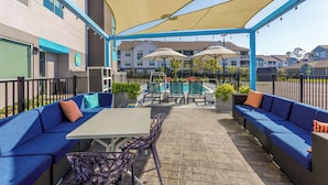 An outdoor patio area with blue sofas, a table, and umbrellas. - Tru By Hilton Panama City Beach (Panama City Beach)