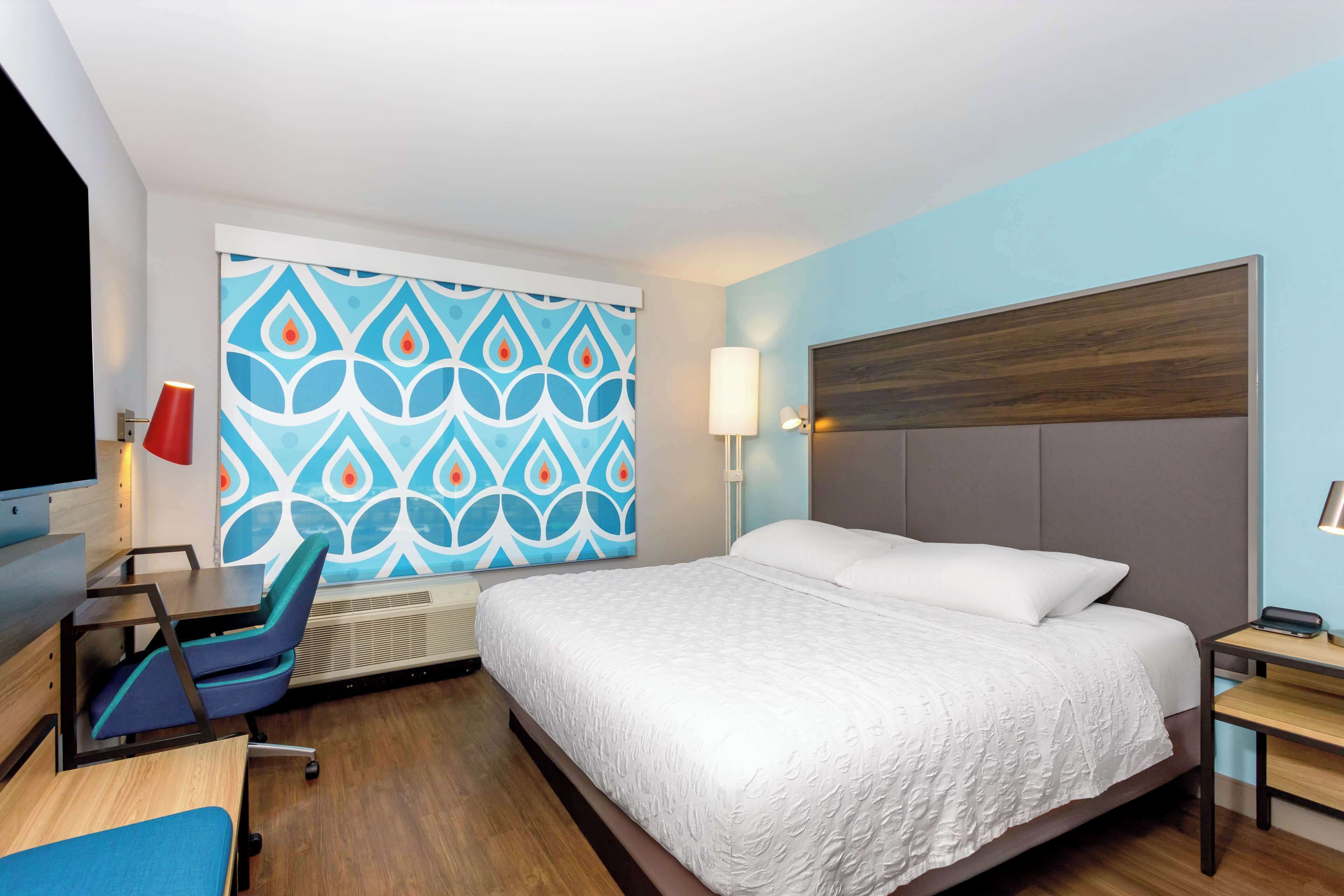 Ein Hotelzimmer mit einem Bett, einem Schreibtisch mit Stuhl, einem Fernseher und einer Wand mit Muster.