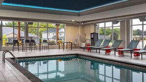 Zona de piscina con sillones reclinables y mesas, ventanas amplias y vistas al vecindario.