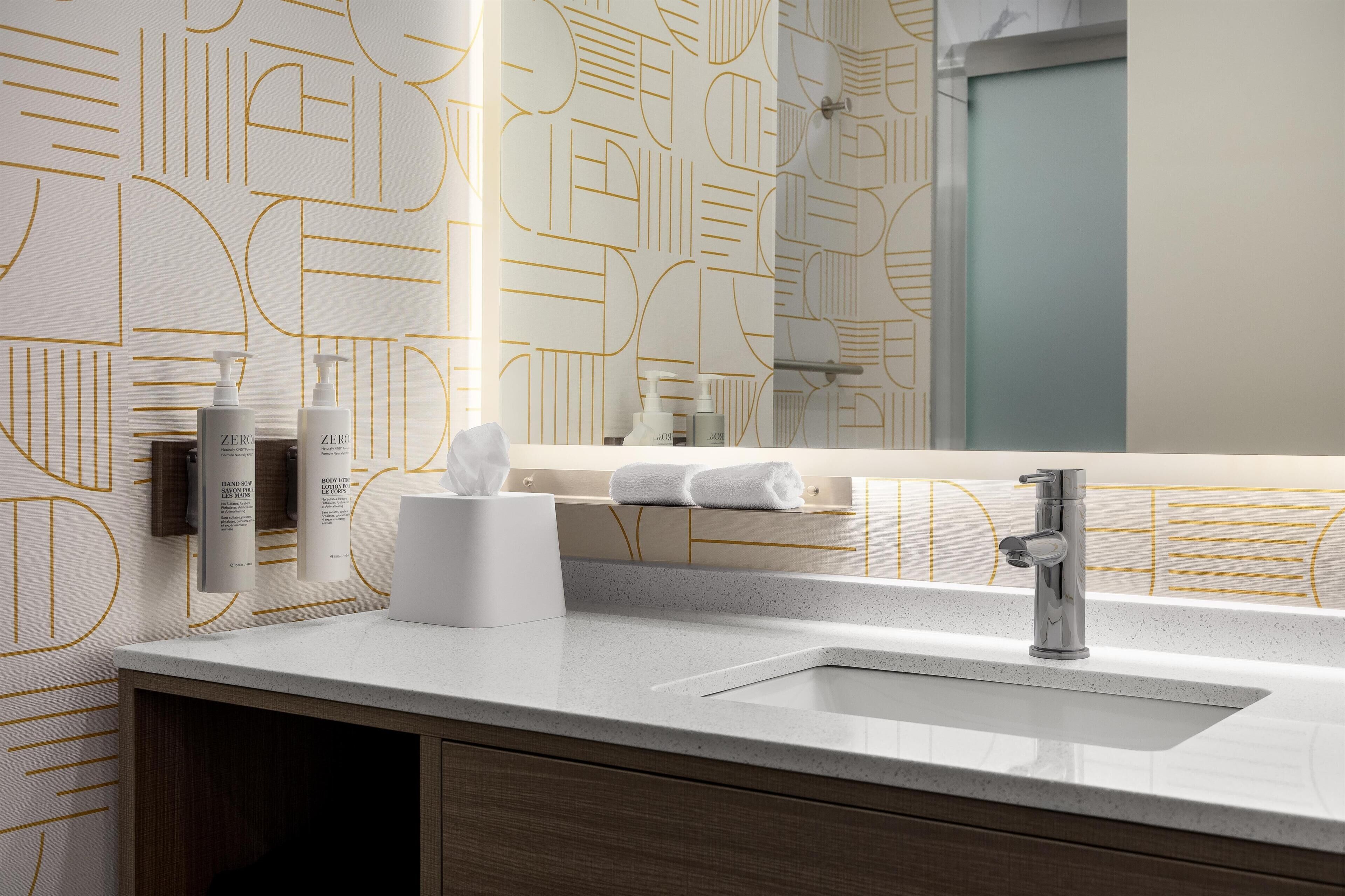 A modern bathroom with a geometric patterned wall, a white sink, and a mirror.
