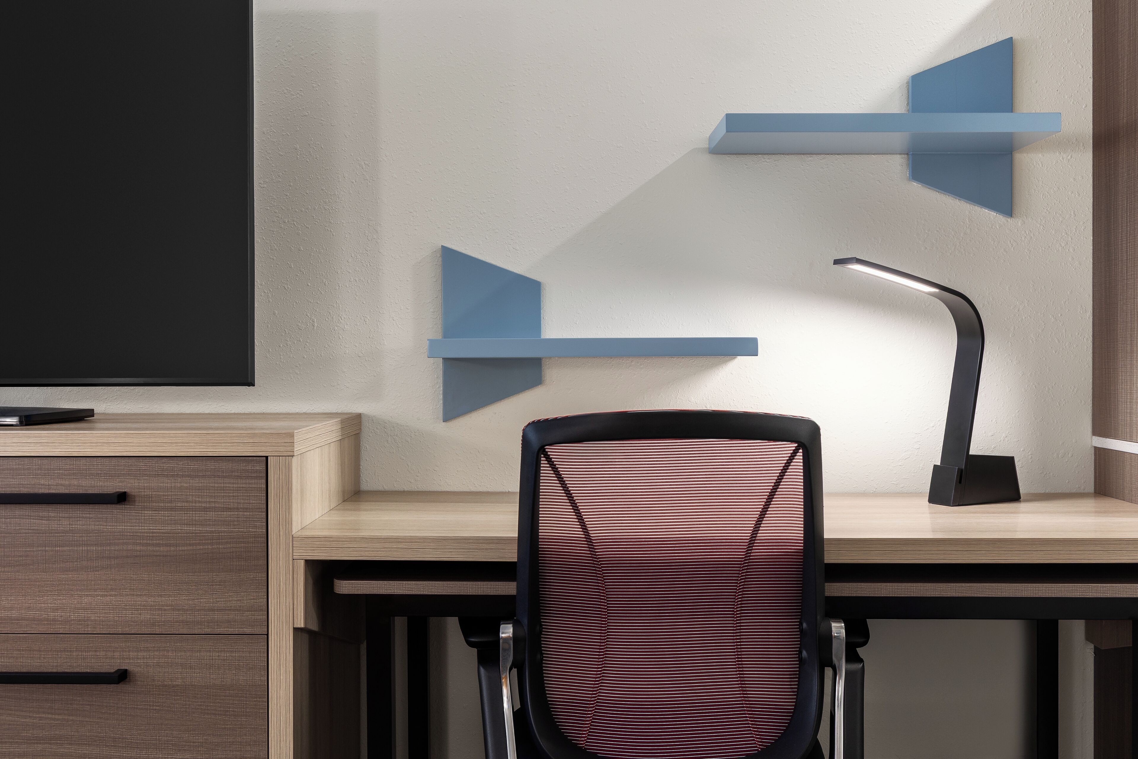Un escritorio moderno con una computadora, una silla y una lámpara de escritorio.