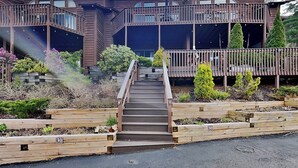 Ein modernes, zweistöckiges Haus mit einer Holzterrasse, einer Treppe zu einer Veranda und einem gepflegten Garten.