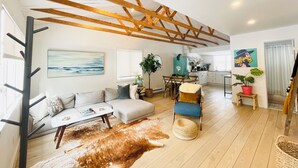 A spacious living area with a high ceiling, wooden beams, a sofa, a dining table, and a kitchen in the background.