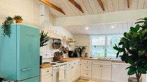 A kitchen with white cabinets, a teal refrigerator, wooden flooring, and a window providing natural light.