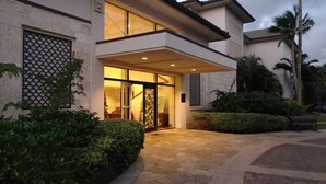 A modern building with a glass entrance, stone pathway, and surrounding greenery.