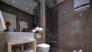 A modern bathroom with a glass-enclosed shower, a white sink, and a toilet. There are towels and toiletries on the shelves. - Via Porto Rooms - Deluxe Room with King Bed (Split)